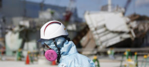 A Tokyo Electric Power Co. (TEPCO) employee, wearing a protective suit and a mask, walks in front of the No. 1 reactor building at TEPCO's Fukushima Daiichi nuclear power plant.  Credit: Toru Hanai/Bloomberg